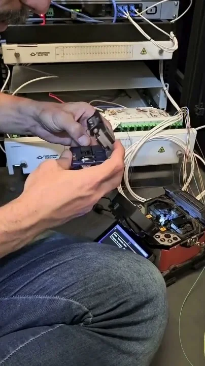Técnico da Lepitel preparando fibra no rack do ponto central, com bandejas do distribuidor óptico Furukawa e máquina de fusão à frente.