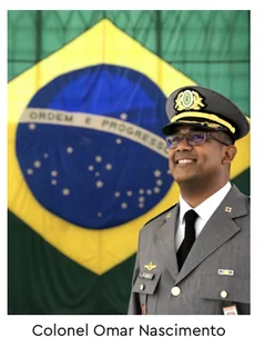 Coronel Omar Nascimento, do Exército Brasileiro, de uniforme e quepe, em frente à bandeira do Brasil.